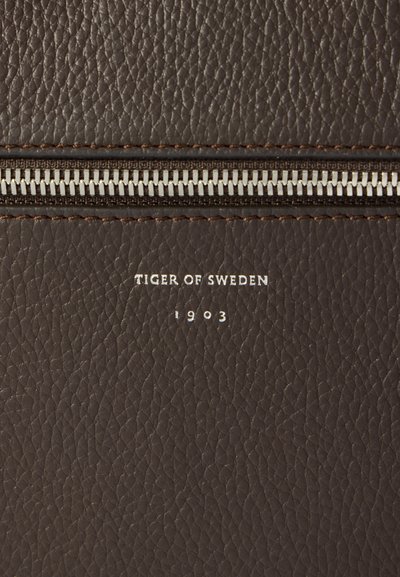 Cartera de cuero marrón texturizado con un cierre de cremallera plateado, nombre de la marca en relieve "Tiger of Sweden" y "1903" en letras blancas.