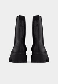 Mustad pahkluu saapad sileda nahkpinnaga, millel on paks, tekstuuriga tald ja õmblustega detailid. Tagaküljel tõmbetõmblused mugavaks jalga panemiseks.