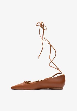Brown leather flat shoe with a pointed toe, featuring a cutout design and long laces for wrapping around the ankle.
