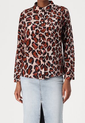 Femme portant une chemise boutonnée à manches longues avec un imprimé léopard rouge et noir associée à une jupe en jean bleu clair avec une fente à l'avant.