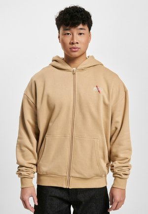 Beige zip-up hoodie made of soft, textured fabric. Features a front pocket and decorative embroidery on the chest. Relaxed fit with a hood.