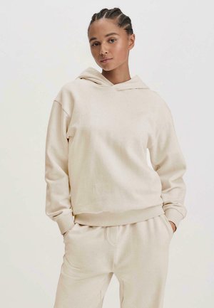 Beiger Kapuzenpullover aus weichem Stoff, mit einer Kängurutasche, gerippten Bündchen und Saum. Tragen mit passenden beigen Jogginghosen.