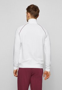 Maglione bianco con collo alto e maniche raglan, impreziosito da dettagli in rosso borgogna. Realizzato in tessuto liscio, presenta una vestibilità comoda.