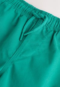 Cintura elástica con cordón atado en pantalones casuales verde azulado hechos de tela suave.