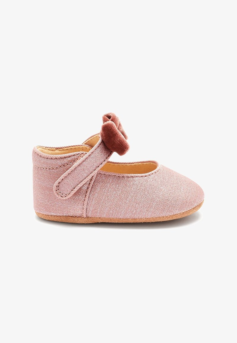 Chaussure en tissu rose avec une texture douce, bout rond et une sangle latérale. Présente une fleur en velours décorative sur la sangle. Semelle flexible.
