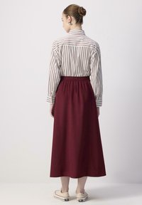 Chemise à manches longues rayée blanc et bordeaux associée à une jupe bordeaux à taille élastique ; la jupe a une texture lisse et un design longueur cheville.