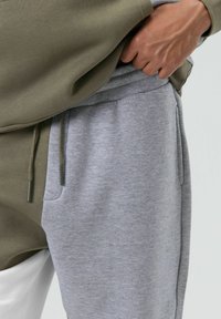 Olifgroene trui met een grote zak, gecombineerd met lichtgrijze joggers met een elastische tailleband en zijzakken.