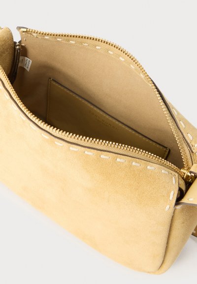 Μπεζ σουέτ τσάντα χιαστί με λευκή ραφή, ανοιχτό φερμουάρ στο πάνω μέρος και ορατή εσωτερική τσέπη.