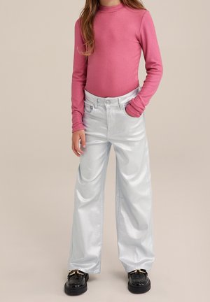 Eng anliegendes pinkfarbenes Langarmshirt mit gerippter Textur; glänzende silberne Schlagjeans mit Taschen und Knopfverschluss; schwarze Schuhe mit metallischen Akzenten.