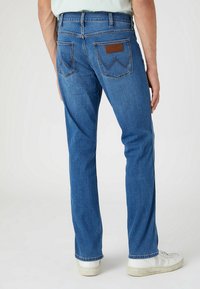 Classic blue denim jeans with a straight-leg design, a leather patch with embossed logo on the back pocket, and subtle stitching details.