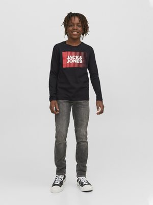 Zwart shirt met lange mouwen met een rood en witte grafische print. G gedragen met grijze jeans en zwart-witte sneakers.