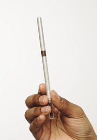 Brunspenne med kropp i sølvfarge og brun tupp, med en uttrekkbar design og en børste i enden for blending, holdt i en hånd.