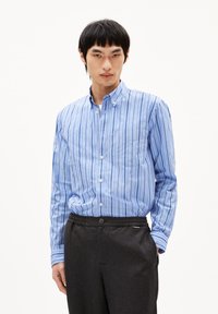 Blauw-witte gestreepte overhemdd met kraag en een zak, gedragen met donkergrijze broek met elastische tailleband. Glad stoftextuur.