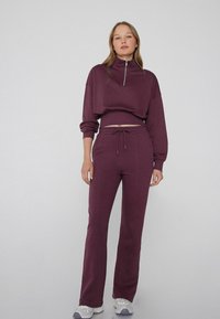 Felpa viola con mezza zip e design cropped, abbinata a pantaloni jogger coordinati con vita regolabile e vestibilità slim.