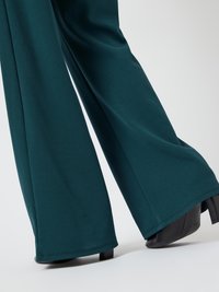 Wijde turquoise broek gemaakt van een gladde stof, met een eenvoudig ontwerp en een nette zoom, gecombineerd met zware zwarte hakken.