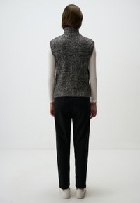 Gilet senza maniche grigio a maglia con colletto alto, tessuto testurizzato, abbinato a pantaloni neri e sneakers bianche, visto da dietro.