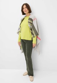 Hellgrüner Pullover kombiniert mit olivgrünen Cordhosen. Ein hellgrauer Schal mit bunten Streifen und Fransendetails. Beigefarbene Mokassins.