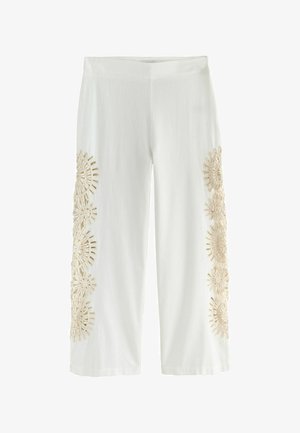 Fehér, rövidített nadrág bézs színű, virágmotívumos csipkemintákkal, amelyek függőlegesen futnak mindkét láb külső oldalán.