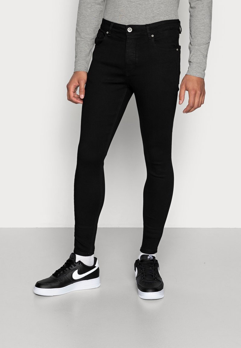 Jeans ajustados de mezclilla negra con una textura suave, diseño de cinco bolsillos, cierre de botón y costuras en contraste. Llevados con zapatillas negras.