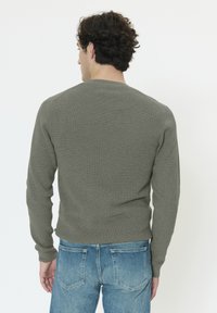 Pull gris à manches longues côtelées avec un col rond, design ajusté et tissu texturé, associé à un jean bleu clair.