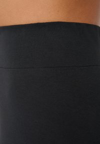 Vêtement en coton noir avec une texture lisse et une large ceinture extensible. Gros plan sur le détail de la ceinture.