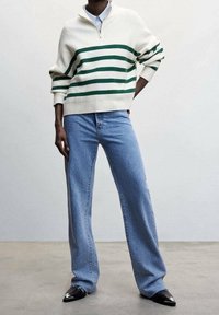Light cream sweater with green stripes, zip collar, paired with light blue wide-leg jeans and black pointed shoes. Smooth, textured fabrics.