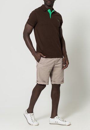 Polo marron avec un col vert, assorti à un short beige. Le mannequin porte des baskets blanches. Coupe décontractée, manches courtes, sans motifs visibles.