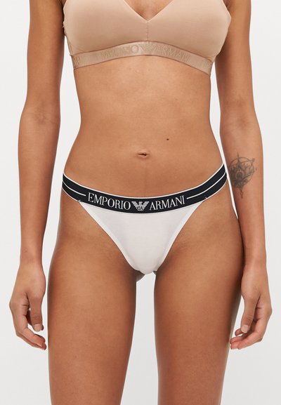 String blanc avec une taille élastique noire portant le logo "EMPORIO ARMANI". Matière en coton douce avec une couverture minimale.