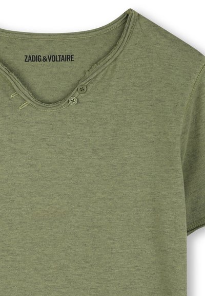 T-shirt vert olive en tissu doux, avec un col rond agrémenté de deux boutons et un léger effilochage au niveau du col. Étiquette de la marque visible.