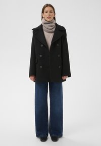 Must, kahekarvaline merepidžaak suurte nööpidega, mida kantakse koos beežika kaelusega ja laiade jalgadega siniste teksapükstega. Sile kangas, soe disain.