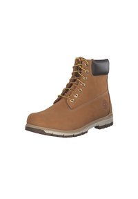 Botas de cuero marrón con cordones, cuello acolchado negro, ojales dorados y suela de goma texturizada. Presenta el logo grabado en el lateral.