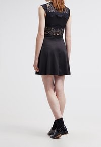 Czarna sukienka z dopasowanym koronkowym topem i rozkloszowaną spódnicą. Charakteryzuje się gładką teksturą i bezrękawowym fasonem. Wykończona prostym obuwiem i skarpetkami.