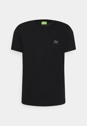 Camiseta de algodón negra con cuello redondo y mangas cortas. Presenta un pequeño parche de logo rectangular en el lado izquierdo del pecho.