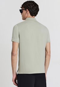Polo en tissu vert clair avec des manches courtes, un col et des fentes sur les côtés. Présentant une texture lisse sans motifs visibles.