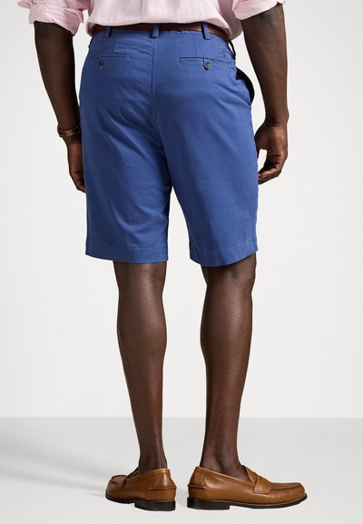 Calças de algodão azuis com um design clean, apresentando bolsos traseiros e uma bainha dobrada, combinadas com sapatos mocassim castanhos.