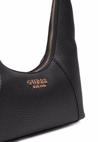 Sac à main en cuir noir avec une forme structurée, doté d'une fermeture éclair en ton or et d'un logo en relief. La surface a une finition texturée.