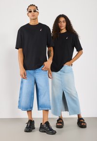 Sorte bomull t-skjorter med en liten hjerte-logo, kombinert med lyseblå vide denimshorts og et langt denimskjørt, begge med et avslappet og ledig snitt.