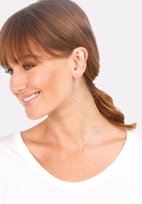 Pendientes de gota plateados con una cadena delgada y un acento redondo y brillante. El diseño simple complementa el escote del portador.
