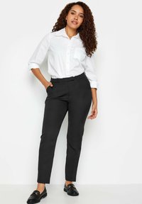 Svarta skräddarsydda byxor i en mjuk tygkvalitet, med midjeband, sidfickor och en smal passform. Kombinerade med en vit skjorta med knappar.