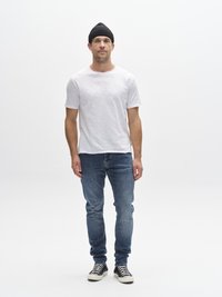 Bela majica s posadko, modre ozke kavbojke, črna kapa in črno-bele superge; preprost dizajn; ravna tekstura na tkanini.