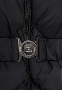 Schwarze Daunenjacke mit einem auffälligen silbernen Metallverschluss, ausgestattet mit einem Reißverschluss und einer gesteppten Textur zur Isolierung.