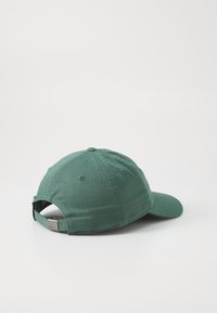 Grønn baseballcap med svingt brisse, laget av stoff med en teksturert overflate. Har en justerbar stropp bak og ventilasjonsøyer.