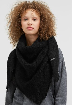 Black triangular scarf made of textured fabric, featuring fringed edges and a small label. Worn over a gray hoodie.