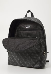 Sac à dos noir avec motif de logo, doté d'une finition lisse, d'une poche zippée à l'avant et d'un intérieur spacieux. Équipé d'une poignée en tissu.