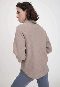 Beiger Fleece-Pullover mit hochgeschlossenem Kragen, überschnittenen Schultern und geradem Saum. Mit einem kleinen Lederakzent auf der Rückseite.