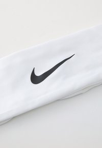 Valge kangast peapael, millel on silmatorkav must Nike' swoosh logo. Disain on sujuv ja sile, sobides ideaalselt sportimiseks.