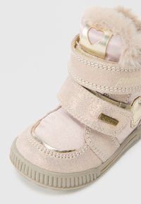 Bota impermeable rosa con borde de piel sintética, dos correas de Velcro, acentos metálicos y suela de goma texturizada. Presenta un detalle en forma de corazón.
