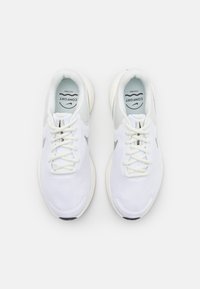 Para białych butów sportowych z jasnoszarymi akcentami, siateczkowymi górnymi częściami i sznurowadłami, widziana z góry na jednolitym białym tle.