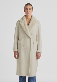 Beige Doppelreiher-Mantel mit einem Pelzkragen und -manschetten, ausgestattet mit zwei Vordertaschen und einem geraden Schnitt. Weiche Stoffstruktur.