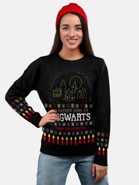 Schwarzer Pullover mit festlichem Design in Weiß, Gelb und Rot, das das Hogwarts-Schloss, Text und Kerzenmuster zeigt. Kombiniert mit einer roten Mütze.